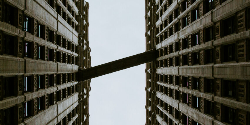 Upward view between the two towers of the Wrigley Building in Chicago, featuring the iconic skybridge and ornate white terracotta detailing.